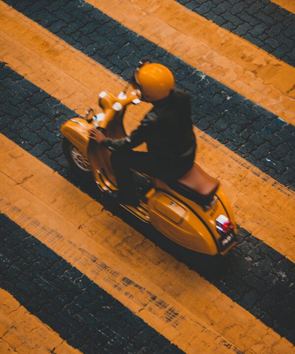 man riding on yellow motor scooter on striped yellow lines