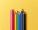 wooden color pencils on yellow paper background, top view
