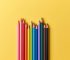 wooden color pencils on yellow paper background, top view